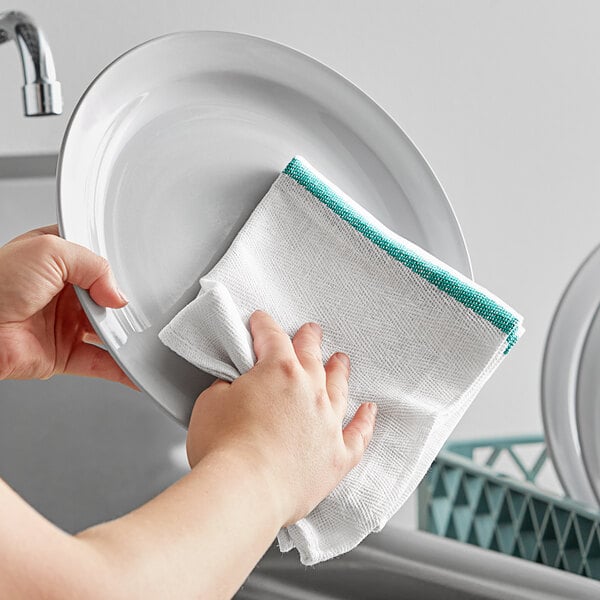 A person wiping a plate with a green-striped herringbone kitchen towel.