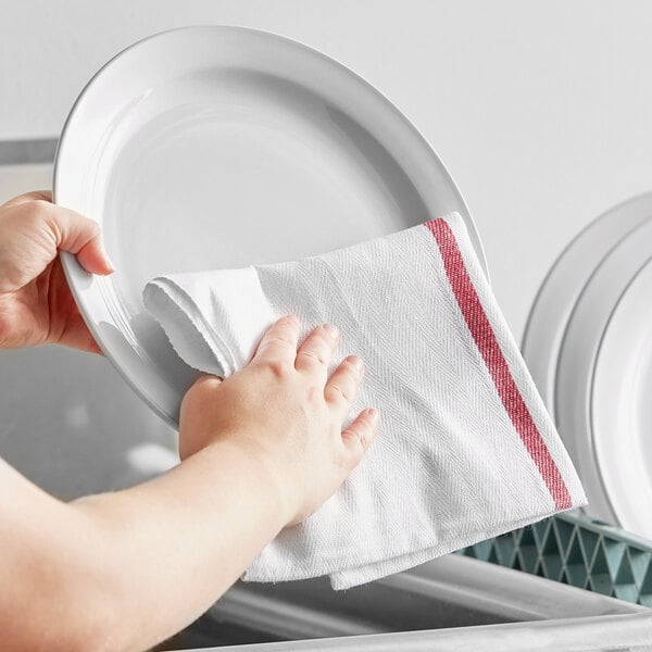 A person wiping a plate with a red-striped Choice kitchen towel.