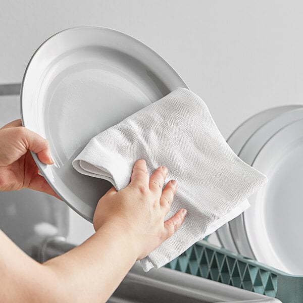 A woman holding a white Choice herringbone kitchen towel over a white plate.