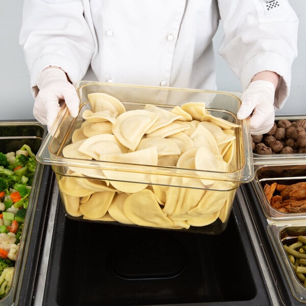 A person in a chef's uniform holding a Cambro amber plastic food pan filled with food.