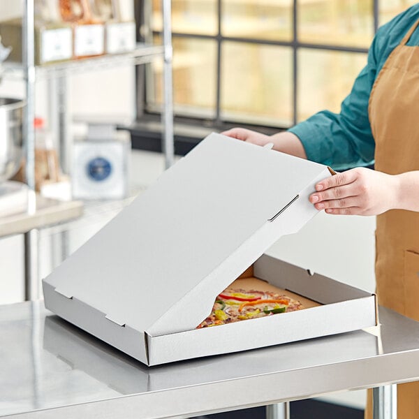 A woman in an apron opening a white customizable corrugated pizza box to reveal a pizza.