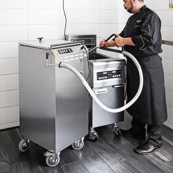 A man in a black uniform using the VITO XL fryer oil filter system in a professional kitchen.