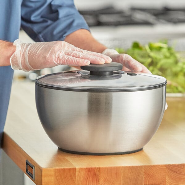 A person in gloves using a stainless steel OXO salad spinner.