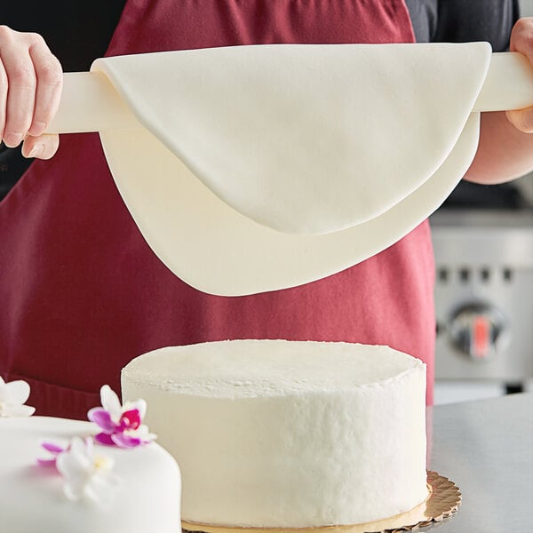 A person using Satin Ice Tropical White Rolled Fondant to decorate a cake with flowers.