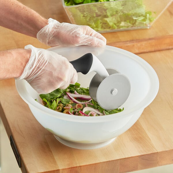 A person using an OXO salad chopper to cut vegetables in a white bowl of salad.