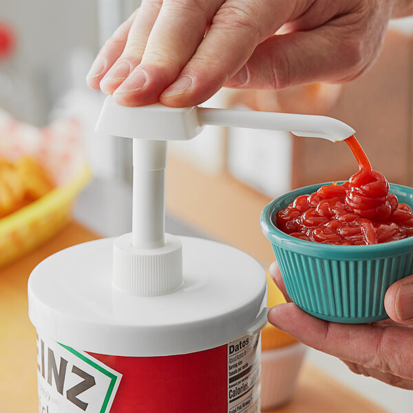 A person using a white plastic pump to pour ketchup into a bowl.