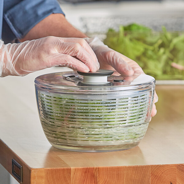 A person wearing gloves and using the OXO Salad Spinner lid to press a button on a container.