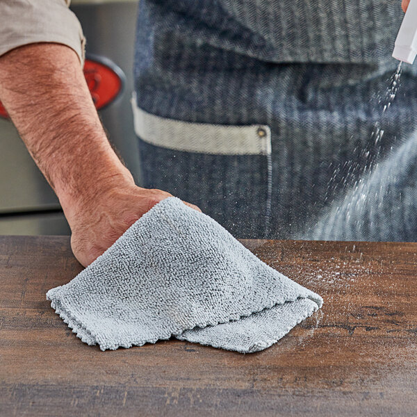 A person using an Unger MicroWipe Pro gray microfiber cloth to clean a wooden table.