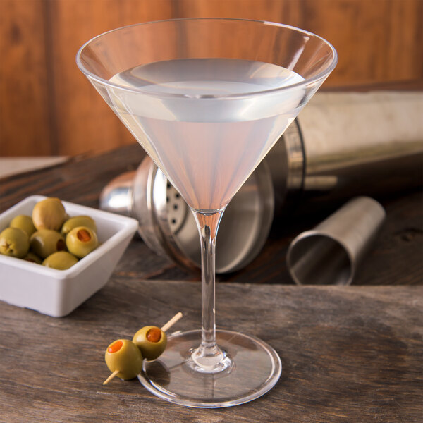 A Carlisle Alibi plastic martini glass filled with a drink and olives on a table.