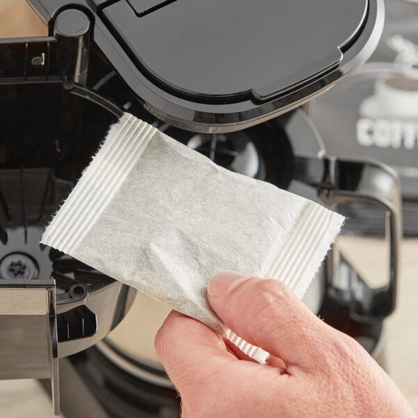 A hand using a white Decaf Room Service 4-Cup Coffee Filter packet to fill a coffee filter.