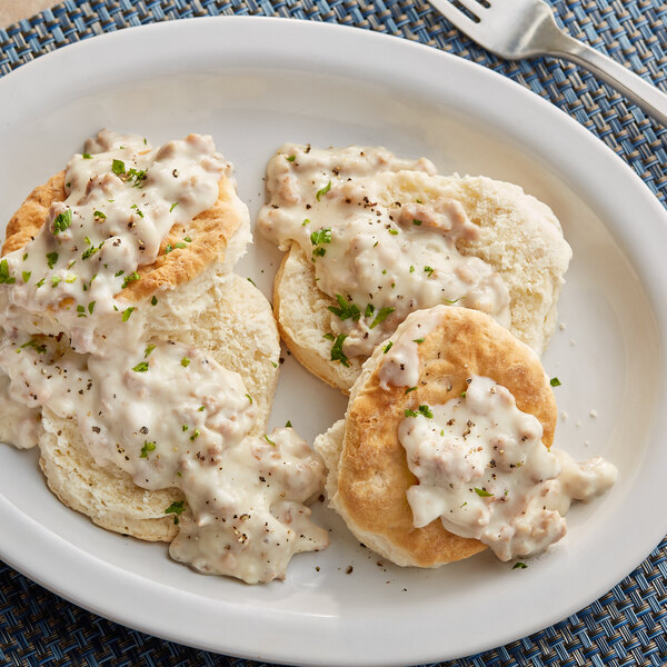 A plate of biscuits and gravy with a fork on a mat.