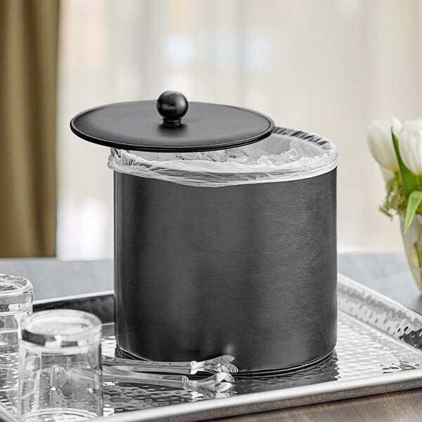 A black Choice insulated ice bucket with a lid on a tray with glasses and a vase of flowers.