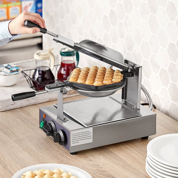 A person using a Carnival King bubble waffle maker on a table with white plates.