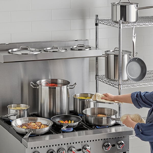 A woman cooking food in Vollrath Optio stainless steel pots and pans on a stove.