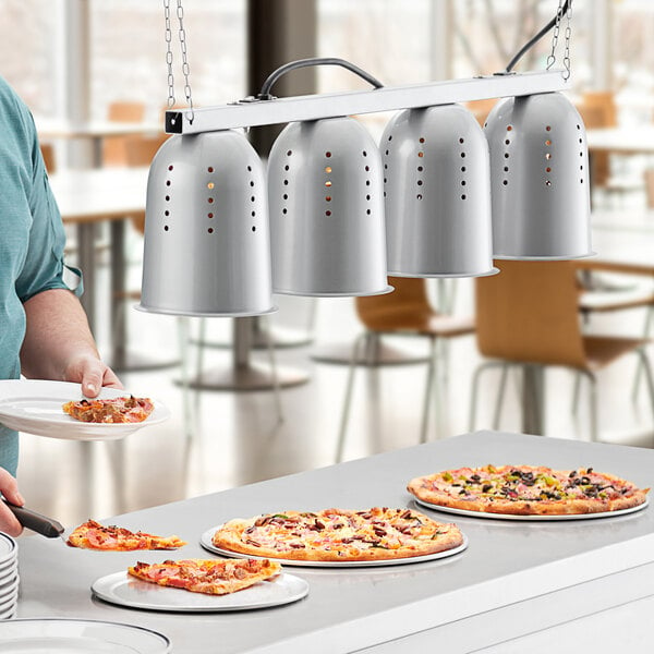 A man using a ServIt hanging heat lamp to serve pizzas on a counter.