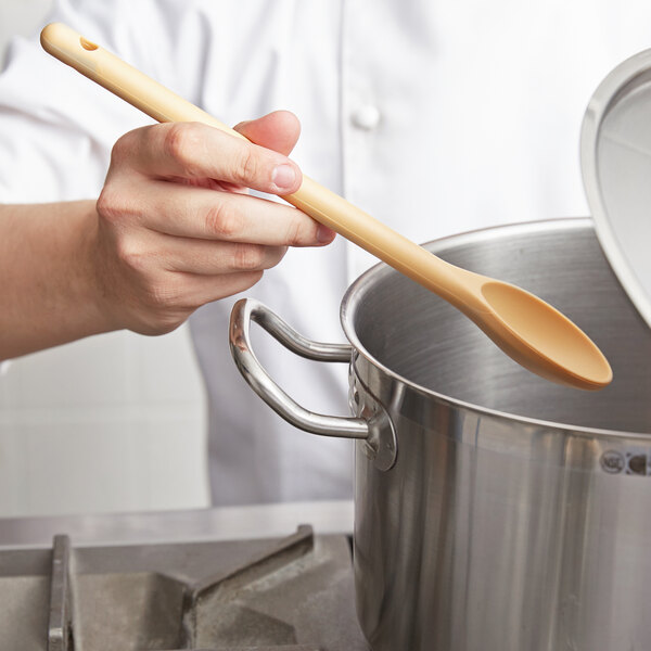 A person stirring a pot of food with a Vollrath tan high heat nylon prep spoon.