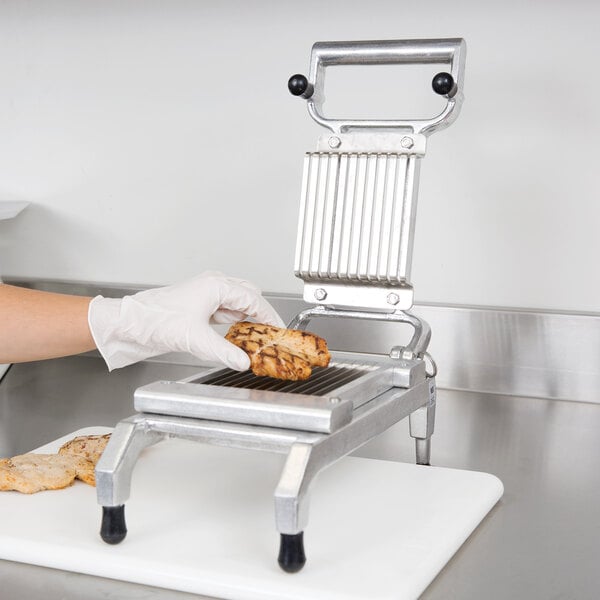 A person in gloves using a Nemco Easy Chicken Slicer to cut a piece of meat.