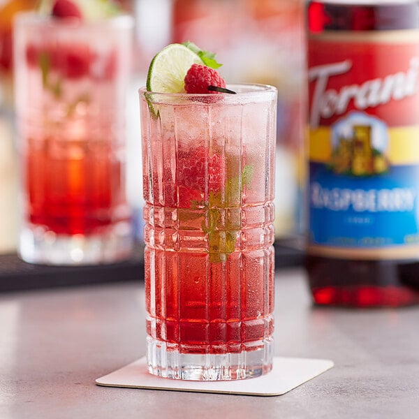 A glass of red drink flavored with Torani Raspberry Syrup with a raspberry on the rim.
