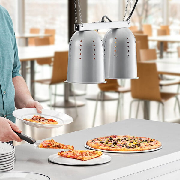 A man using a ServIt hanging heat lamp to keep pizza warm on plates.