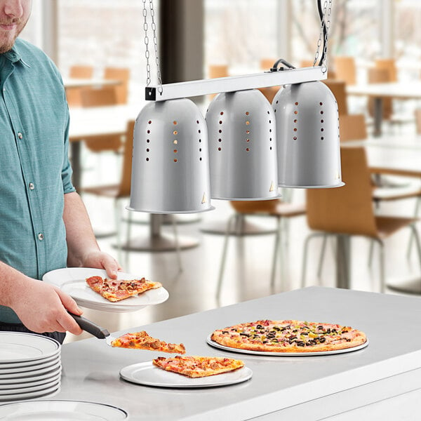A man using a ServIt hanging heat lamp to keep pizza warm on a counter.