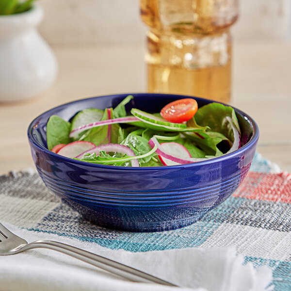 An Acopa Capri deep sea cobalt stoneware bowl filled with salad and vegetables on a table in a salad bar.