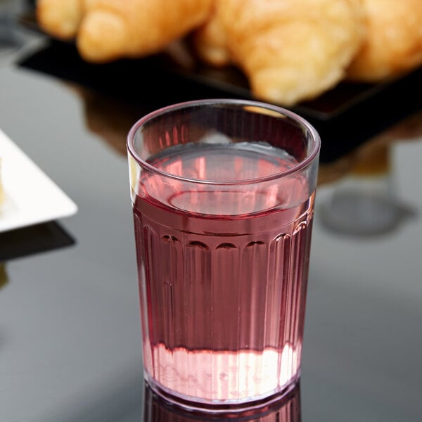 A Carlisle clear plastic tumbler filled with pink liquid on a table with croissants.