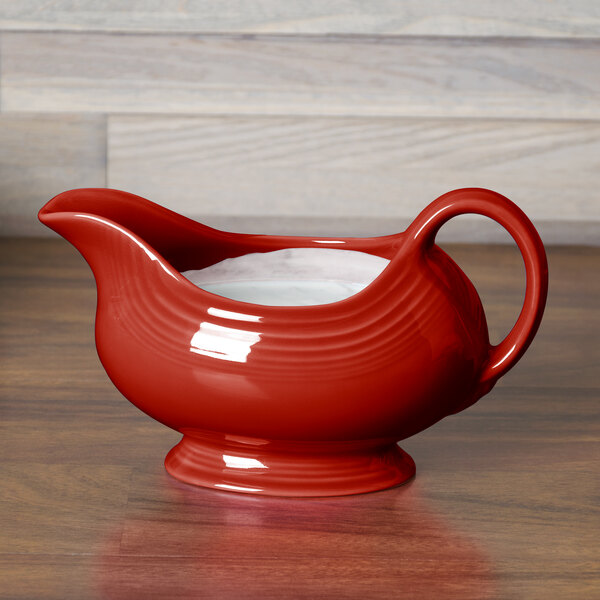 A Scarlet Fiesta gravy boat with a handle on a wood surface.
