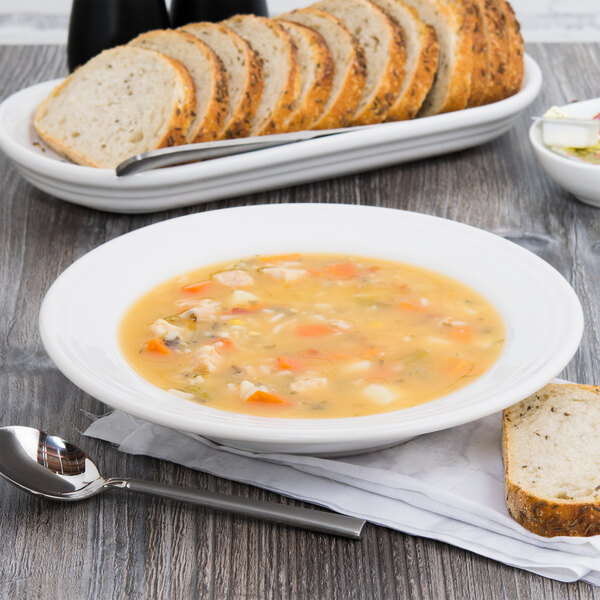 A white Fiesta china rim soup bowl filled with soup next to a plate of bread.