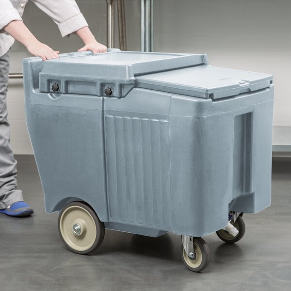 A person pushing a large grey Cambro Mobile Ice Bin with wheels.