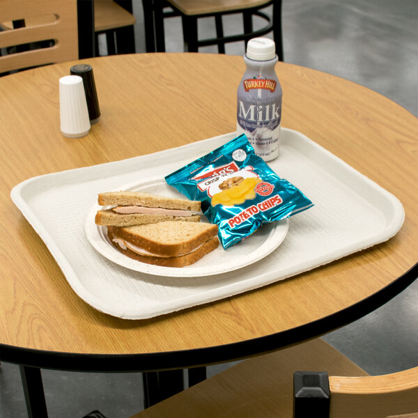 A Huhtamaki Chinet rectangular paper food tray with sandwiches and chips on a table.