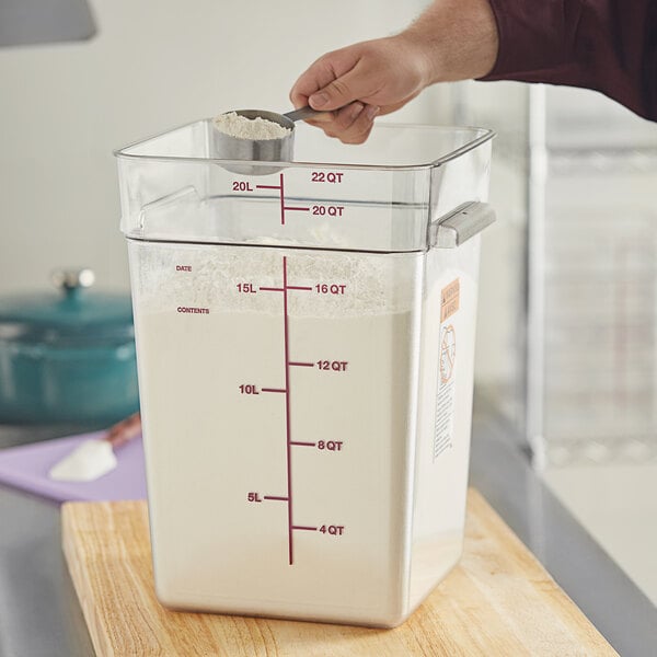A person using a Vigor clear square food storage container to measure white flour.
