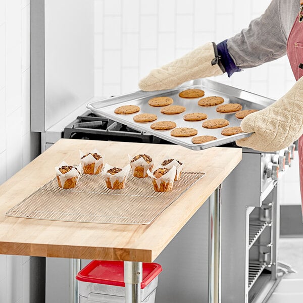 A woman in an apron holding a Baker's Mark wire-in-rim aluminum sheet pan with cookies on a counter.