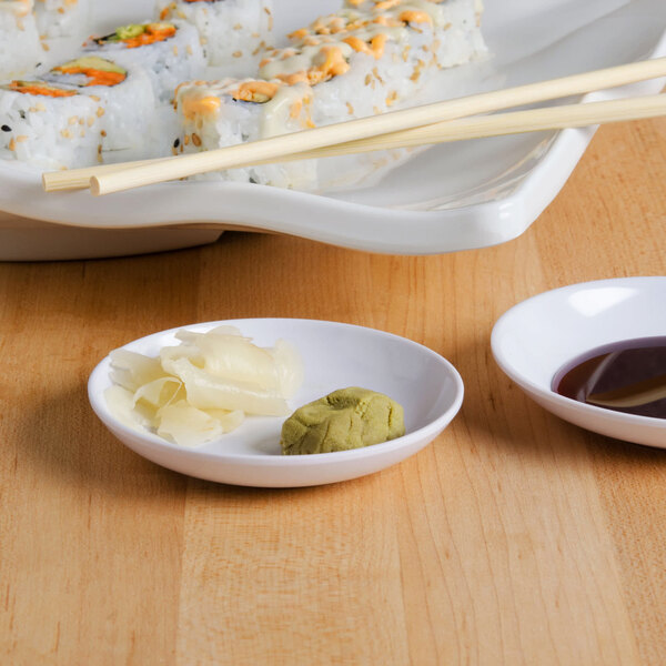 A white sauce dish filled with brown sauce next to sushi on a plate.