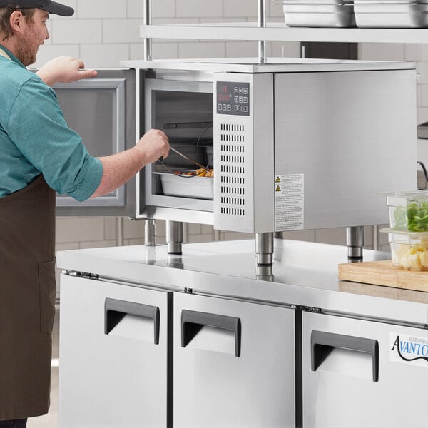 A man in an apron opening an Avantco countertop blast chiller in a professional kitchen.