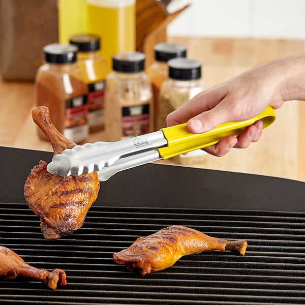 A person using Choice yellow stainless steel scalloped tongs to grill chicken.