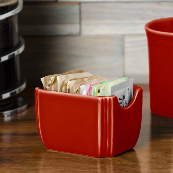 A red Fiesta sugar caddy on a counter with sugar packets inside.