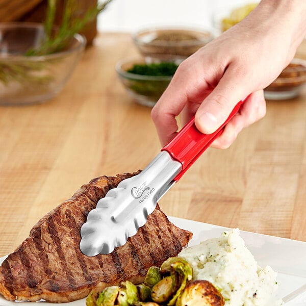 A person using Choice red stainless steel tongs to serve a steak.