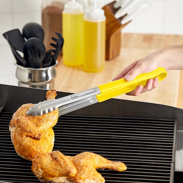 A person using Choice yellow and silver stainless steel scalloped tongs to grill chicken.