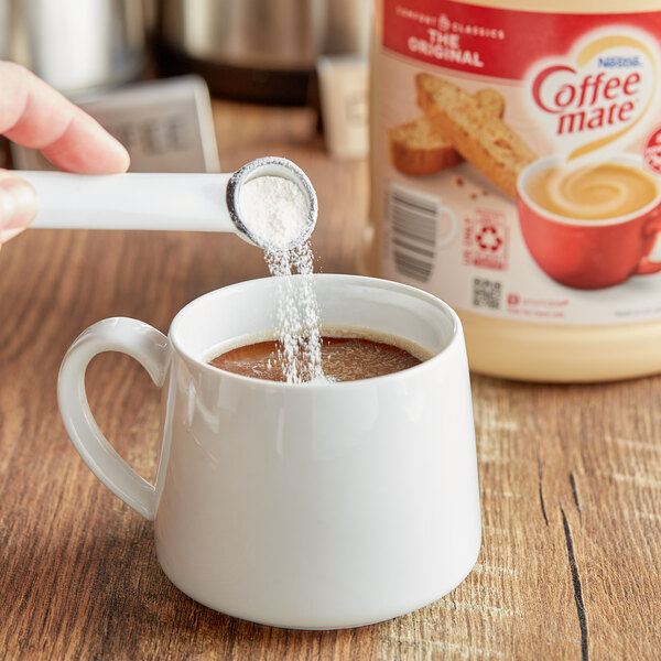 A person pouring Nestle Coffee-Mate Original powder into a cup of coffee.