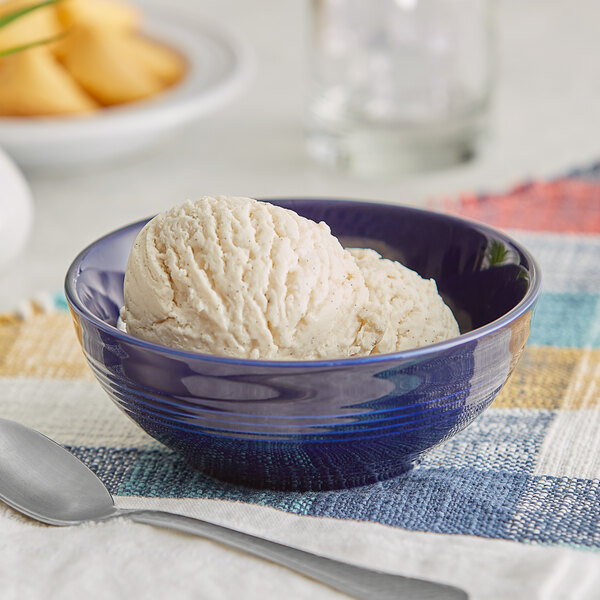 A deep sea cobalt Acopa Capri stoneware nappie bowl filled with ice cream on a table.