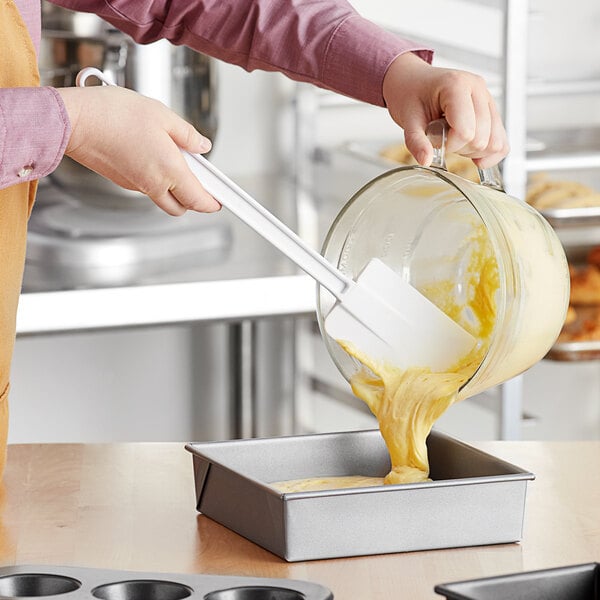 A person using a Choice white spatula to put batter in a baking dish.