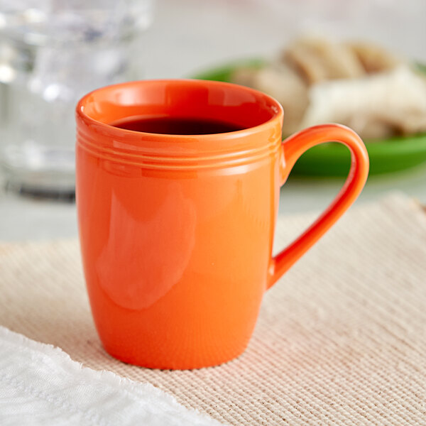 An orange mug with a handle on a table with a green plate of food.