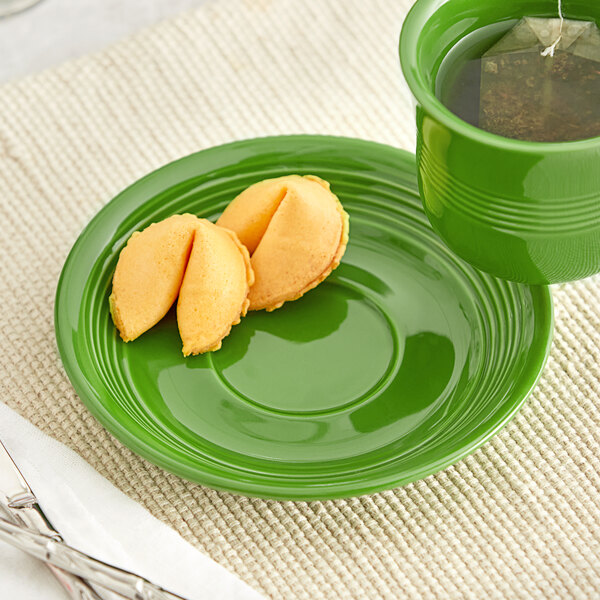 A green Acopa Capri stoneware saucer with a cup of tea and fortune cookies.