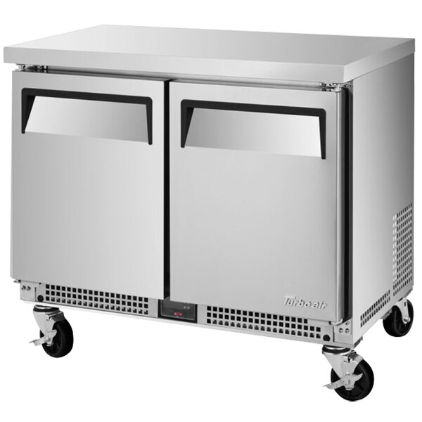 A silver Turbo Air undercounter refrigerator with solid doors and wheels.