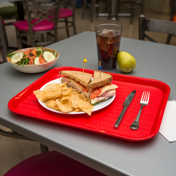 A Carlisle red fast food tray with a sandwich and chips on it.