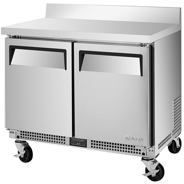 A silver stainless steel Turbo Air worktop refrigerator with black wheels.