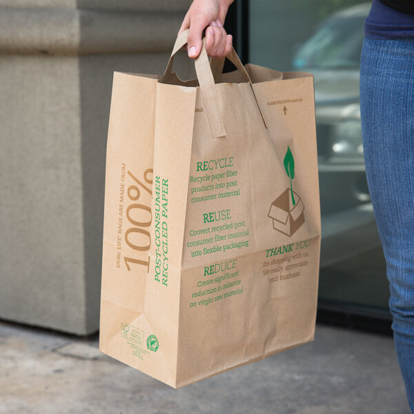 A person holding a Duro brown paper shopping bag with green text.