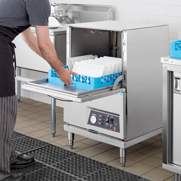 A man putting a blue tray into a Noble Warewashing undercounter dishwasher.