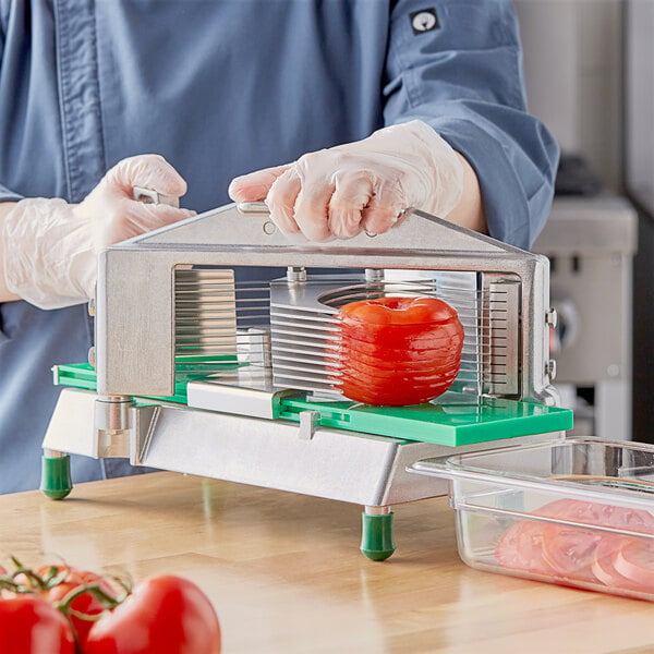 A person in gloves using a Garde 7/32" tomato slicer to cut a tomato on a cutting board.