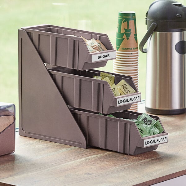 A brown plastic 3-tier organizer set with bins and labels holding packets.